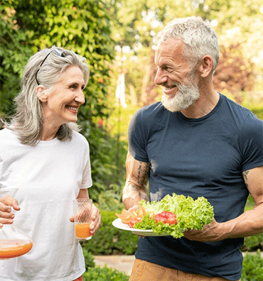 Two older adults sharing a fresh salad and drinks outdoors in a garden