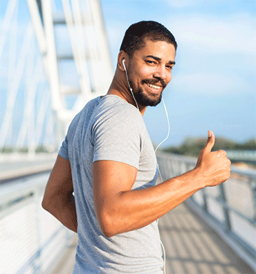 Person jogging outdoors with earphones and giving a thumbs-up on a modern bridge