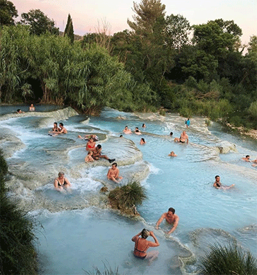 People bathing in natural sulfur thermal pools surrounded by lush vegetation in Italy
